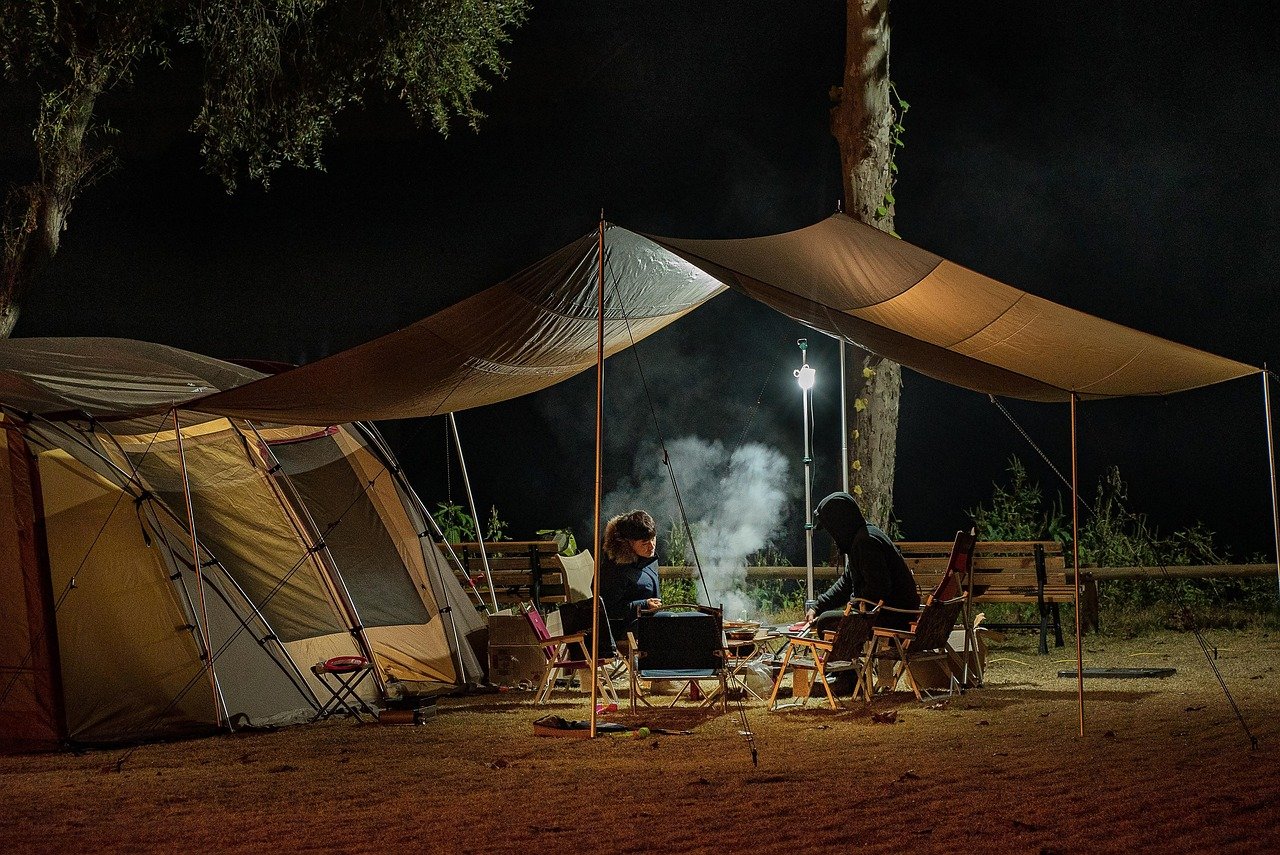 wo people relaxing at a campsite at night under a tarp after completing a micro workout outdoors.
